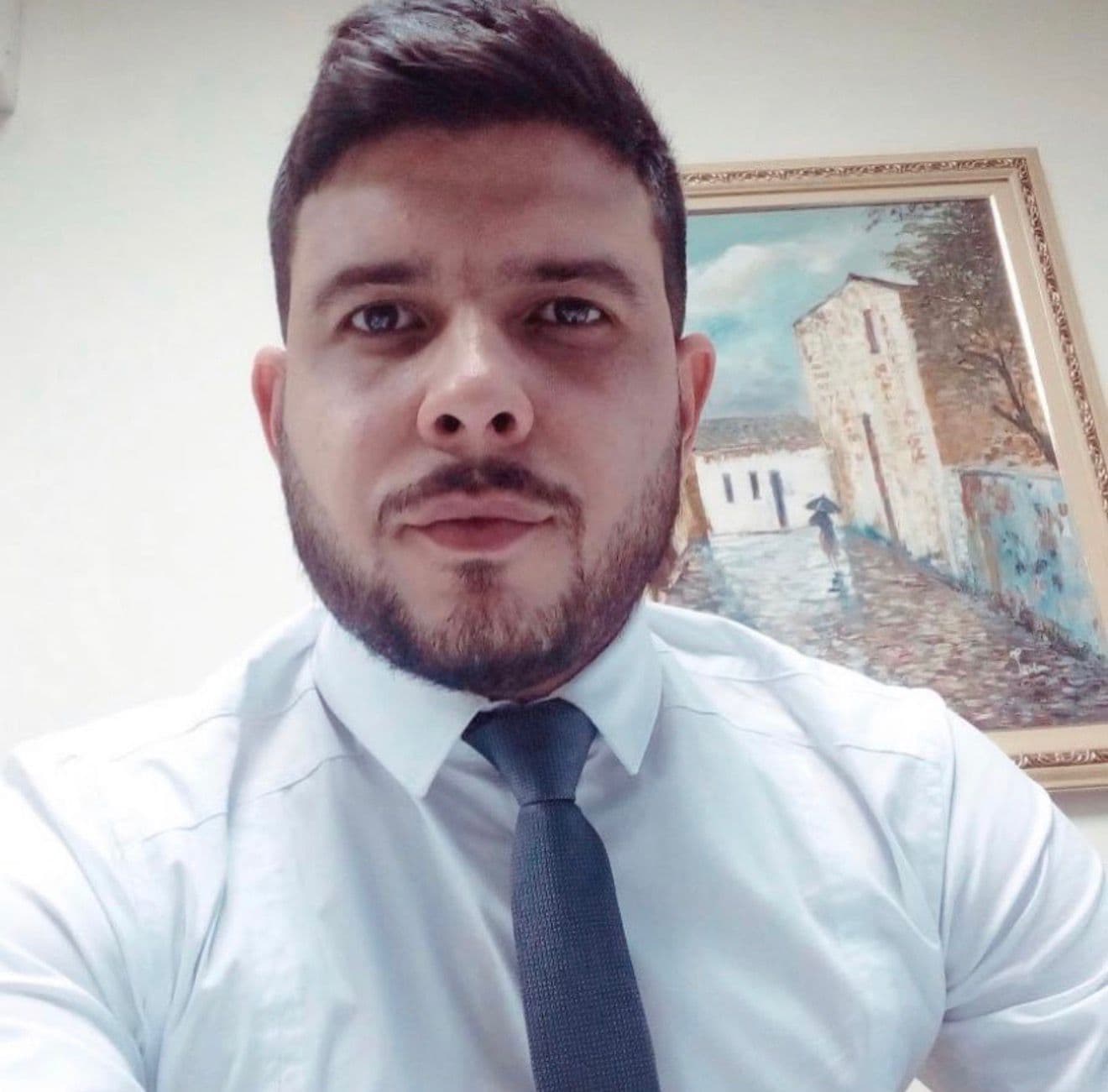 Bearded man in white shirt and dark tie, with a framed street scene painting.